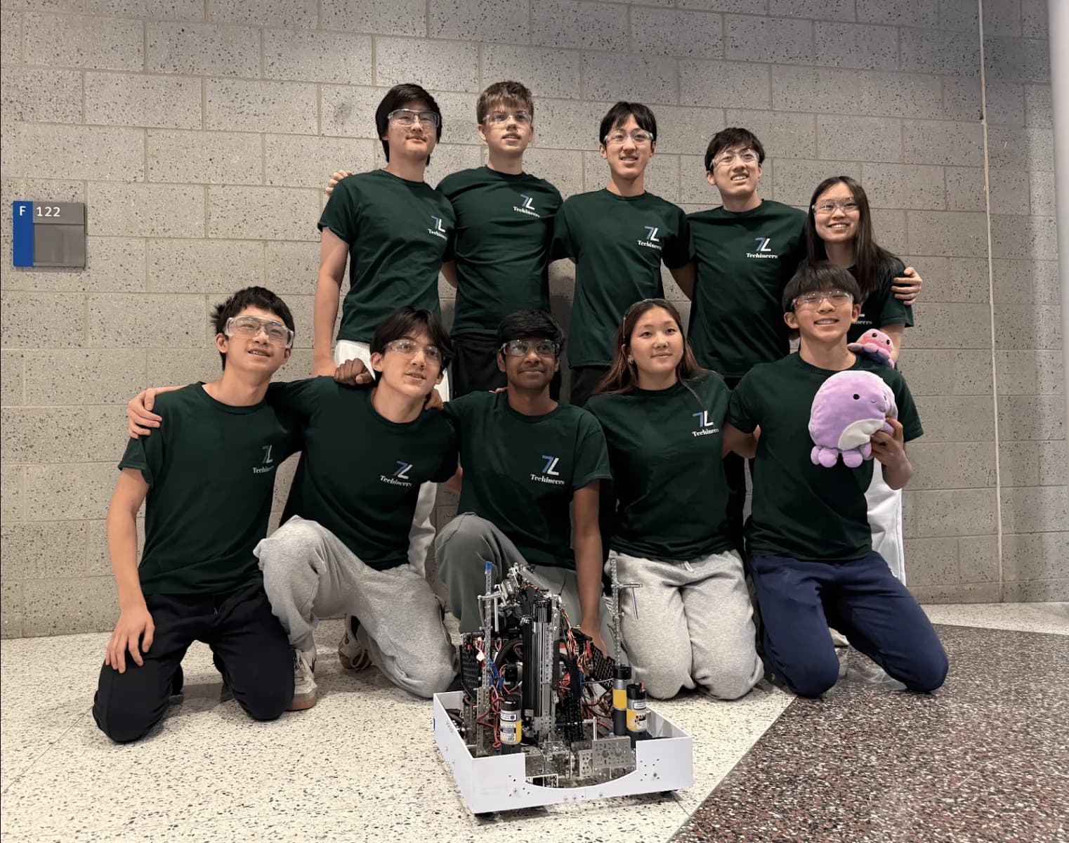 The 2024-25 Techineers in green shirts kneeling and standing around Rob-Ot